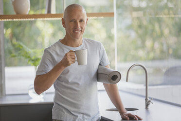 Portrait lächelnder reifer Mann mit Yogamatte trinkt Kaffee in der Küche - HOXF02042