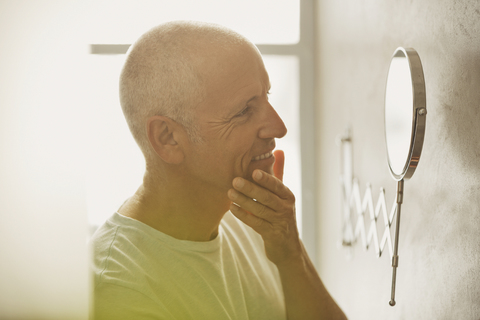 Älterer Mann betrachtet Haut in Vergrößerungsspiegel im Badezimmer, lizenzfreies Stockfoto