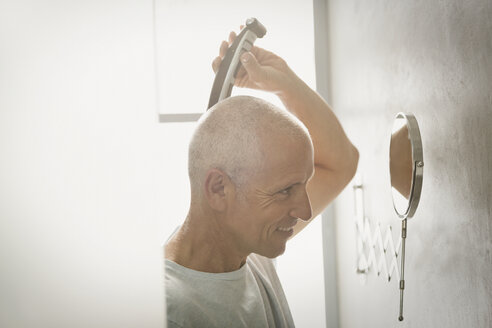 Älterer Mann rasiert sich den Kopf mit einem elektrischen Rasierapparat im Badezimmer - HOXF02054