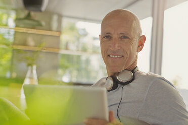 Porträt lächelnder reifer Mann mit Kopfhörern und digitalem Tablet - HOXF02063