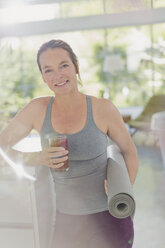 Portrait lächelnde reife Frau mit Yogamatte trinkt Saft Smoothie - HOXF02067