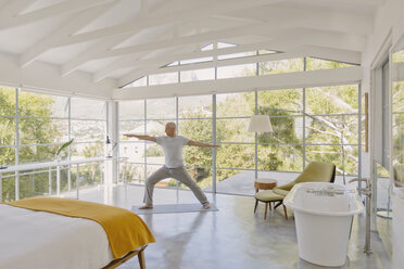 Älterer Mann übt Yoga Krieger 2 Pose in Luxus-Schlafzimmer - HOXF02068