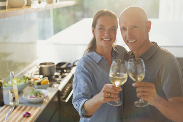 Portrait happy mature couple toasting white wine glasses, cooking in kitchen - HOXF02089