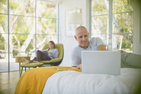 Älteres Paar entspannt sich, benutzt Laptop und Tablet im Schlafzimmer, lizenzfreies Stockfoto