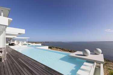 Sunny, tranquil modern luxury home showcase exterior infinity pool with ocean view under blue sky - HOXF02097