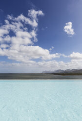 Sonniger, ruhiger Infinity-Pool mit Meerblick unter blauem Himmel mit Wolken - HOXF02099