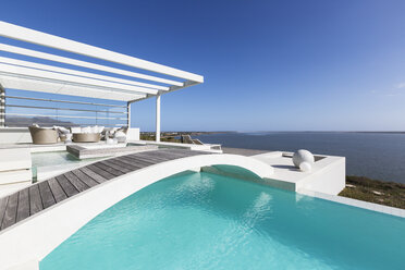 Sunny tranquil home showcase exterior infinity pool with ocean view under blue sky - HOXF02113