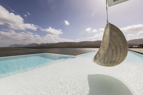 Sonnige, ruhige Luxus-Terrasse mit Infinity-Pool und Hängesitz mit Meerblick, lizenzfreies Stockfoto