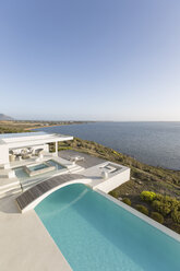 Sunny, tranquil modern luxury home showcase infinity pool with footbridge and ocean view under blue sky - HOXF02154