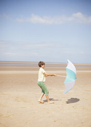 Wind zieht Regenschirm in den Händen eines Jungen am sonnigen Sommerstrand - HOXF02171