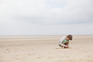 Boy playing in sand on overcast summer beach - HOXF02175