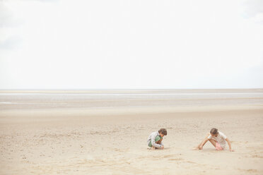 Bruder und Schwester spielen im Sand am bedeckten Sommerstrand - HOXF02183