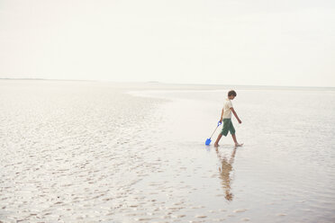 Junge geht mit Schaufel in nassem Sand an einem bewölkten Sommerstrand - HOXF02192
