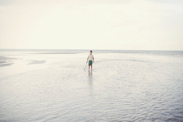 Portrait boy holding shove in ocean surf on overcast summer beach - HOXF02193