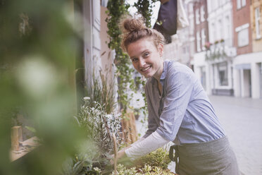 Porträt einer lächelnden jungen Blumenhändlerin, die eine Auslage im Geschäft arrangiert - HOXF02198