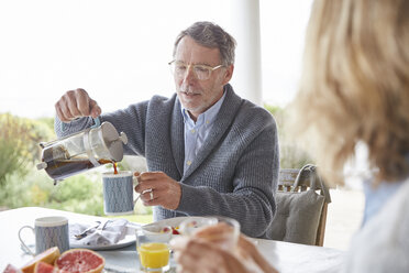 Älterer Mann gießt auf der Terrasse Kaffee aus einer French Press ein - HOXF02237