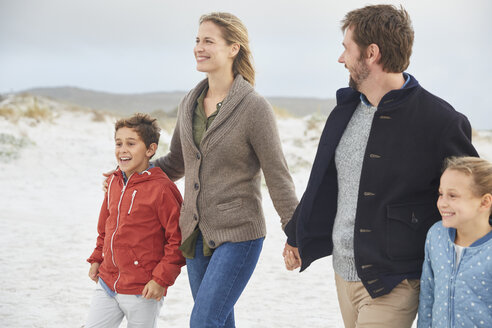 Familie hält sich an den Händen und geht am Winterstrand spazieren - HOXF02252