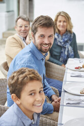 Porträt einer lächelnden Mehrgenerationenfamilie beim Mittagessen im Innenhof - HOXF02256
