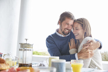 Smiling affectionate couple hugging at patio breakfast table - HOXF02274