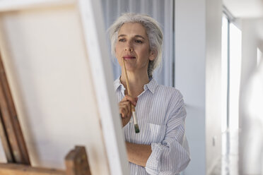 Pensive mature woman painting at easel - HOXF02285