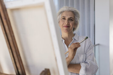 Portrait confident mature woman painting at canvas on easel - HOXF02303