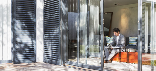 Businesswoman working in living room open to sunny patio - HOXF02358