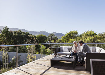 Businessman and businesswoman working on sunny luxury balcony patio sofa - HOXF02364