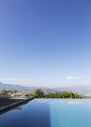 Ruhiger, luxuriöser Infinity-Pool mit Blick auf die Berge unter sonnigem, blauem Himmel - HOXF02381