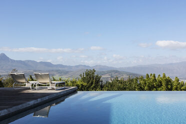 Luxuriöser Infinity-Pool und Liegestühle mit Bergblick unter sonnigem, blauem Himmel - HOXF02397