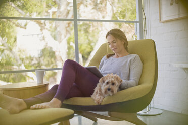 Frau mit Hund, die sich auf einem Stuhl mit digitalem Tablet entspannt - HOXF02403