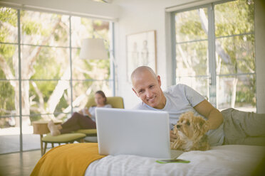 Lächelnder Mann mit Hund am Laptop auf dem Bett - HOXF02404