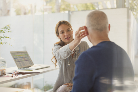 Female doctor helping male patient with hearing aid in doctor’s office stock photo