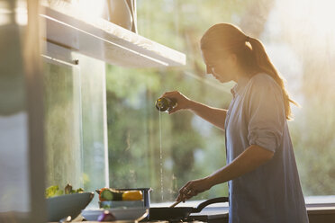 Woman pouring oil into pan on stove in kitchen - HOXF02424