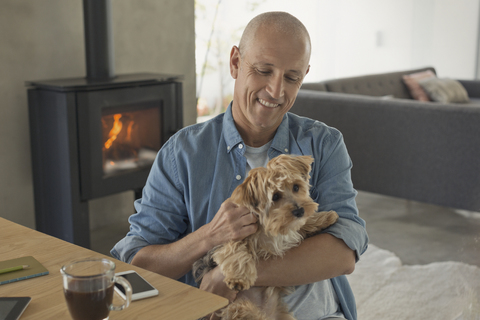 Lächelnder Mann streichelt Hund vor dem Holzofen Kamin, lizenzfreies Stockfoto