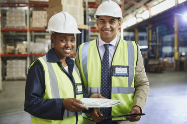 Portrait smiling manager and worker with paperwork in distribution warehouse - HOXF02445