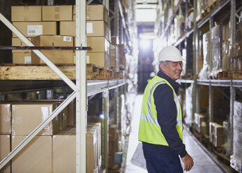 Portrait smiling worker in distribution warehouse aisle - HOXF02447