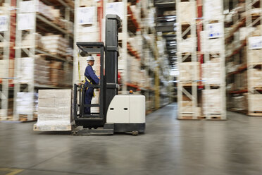 Worker operating forklift moving pallet of boxes in distribution warehouse - HOXF02468