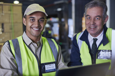 Porträt eines lächelnden Managers und eines Arbeiters, der einen Laptop in einem Vertriebslager benutzt - HOXF02475