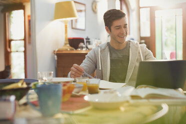 Junger Mann, College-Student, der beim Frühstück einen Laptop benutzt - HOXF02492