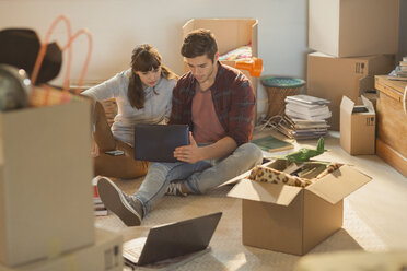 Young couple using laptop surrounded by moving boxes - HOXF02494