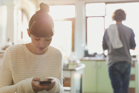 Junge Frau, die in der Küche mit ihrem Handy SMS schreibt, lizenzfreies Stockfoto