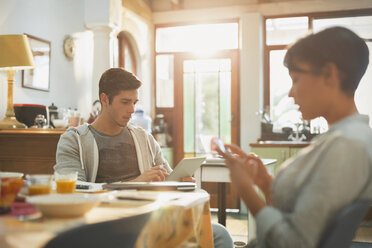 Young couple college students using cell phone and digital tablet at kitchen table - HOXF02510