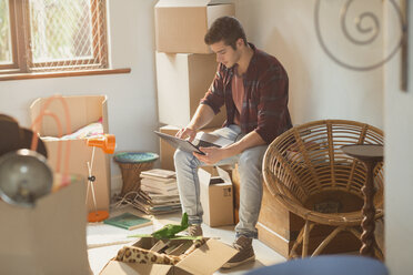 Junger Mann mit Laptop, umgeben von Umzugskartons in einer Wohnung - HOXF02511