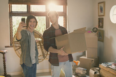Young men roommates taking selfie moving boxes in apartment - HOXF02517