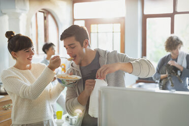 Junge Frau füttert ihren Freund mit Müsli in der Wohnküche - HOXF02520