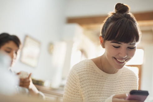 Lächelnde junge Frau, die eine SMS mit ihrem Handy schreibt - HOXF02556