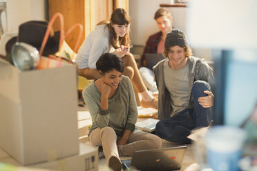 Junge Paare, die einen Laptop benutzen, um Umzugskartons in einer neuen Wohnung auszupacken - HOXF02583