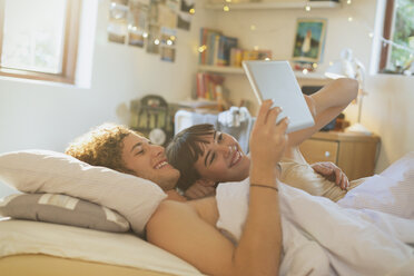 Smiling young couple laying in bed using digital tablet - HOXF02591