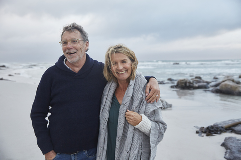 Portrait lächelndes älteres Paar, das sich am stürmischen Strand umarmt, lizenzfreies Stockfoto