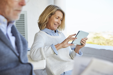 Ältere Frau benutzt digitales Tablet auf der Terrasse, lizenzfreies Stockfoto